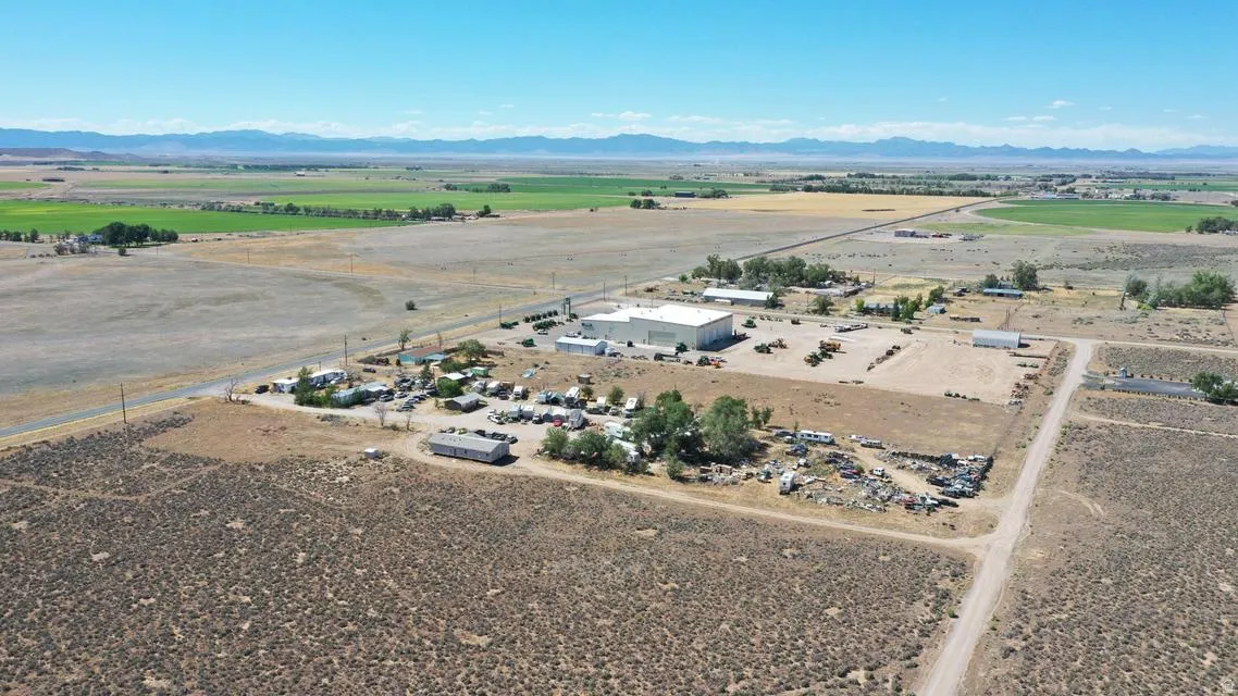 Expansive property featuring a large industrial-style building with a light-colored roof, multiple outbuildings, and extensive open land