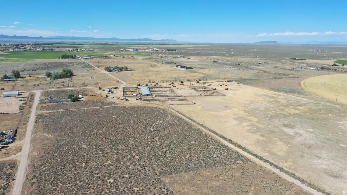 Expansive rural landscape featuring a large open field, several outbuildings, and distant mountain ranges