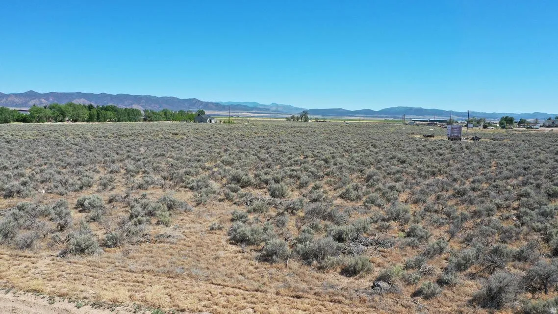 Expansive, undeveloped land featuring natural shrubbery and distant mountain ranges under a clear sky