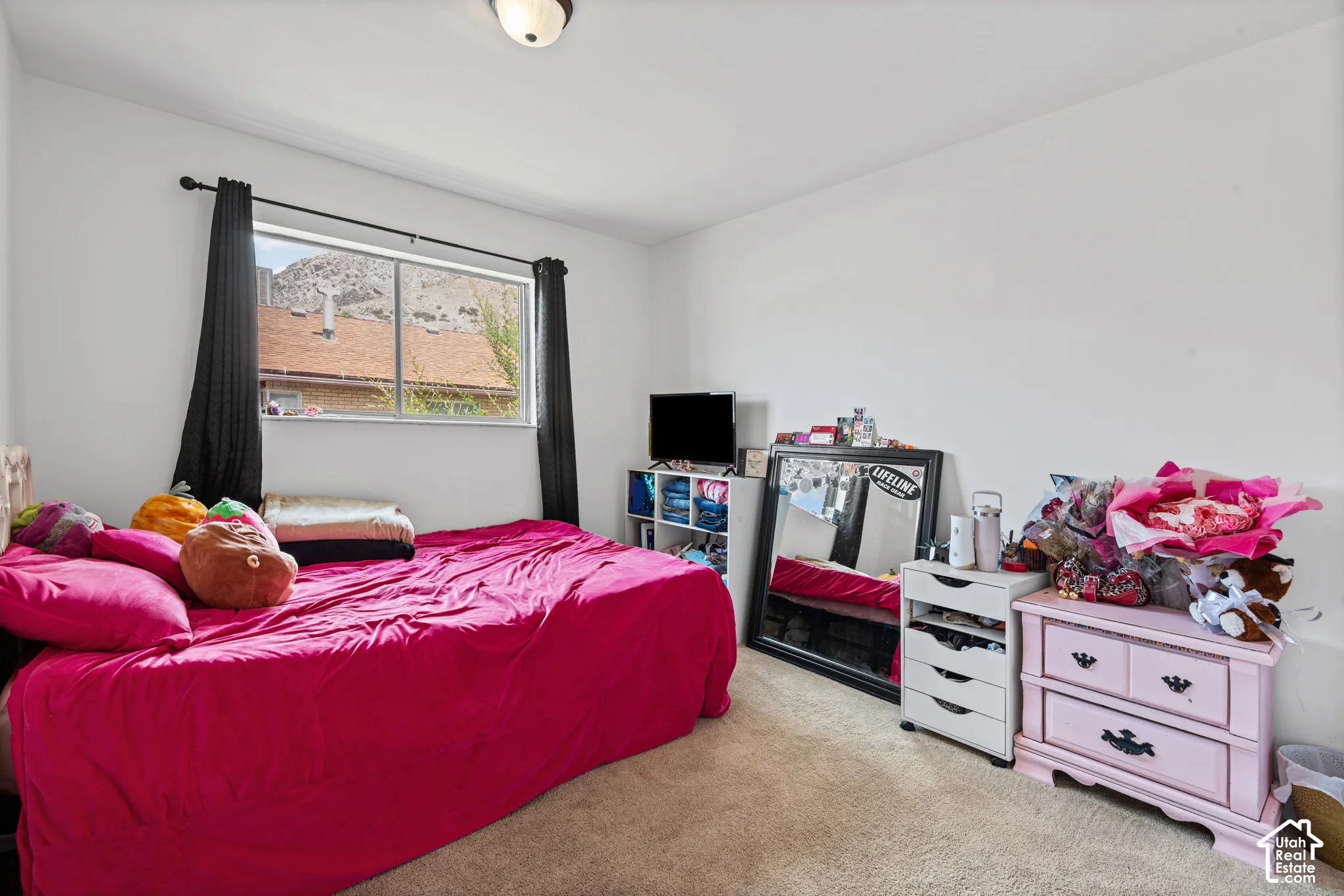 Carpeted bedroom featuring a single window with dark drapery, white walls, and a ceiling-mounted light fixture