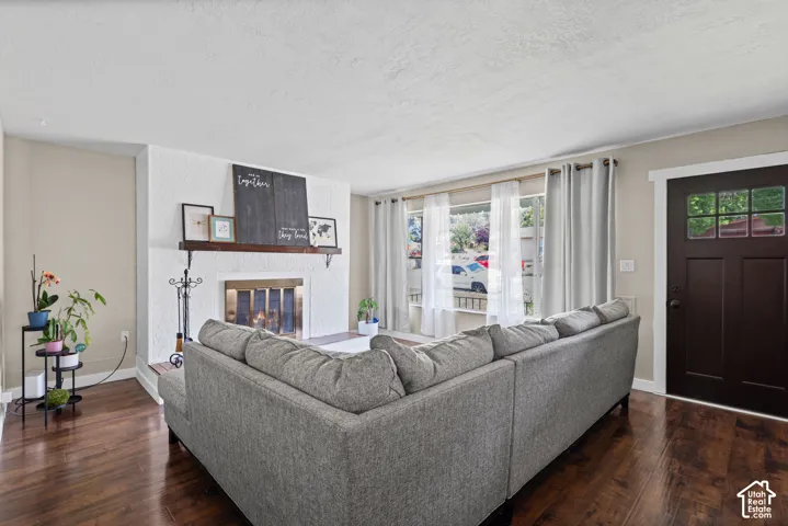 Living area featuring wood-finish flooring, a white textured fireplace, a dark wood mantel, and large picture windows