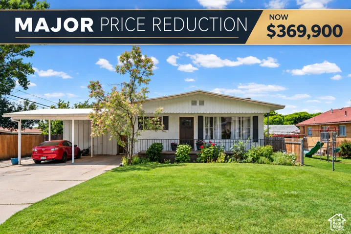 White exterior with dark shutters, front landscaping, covered carport, and expansive front lawn