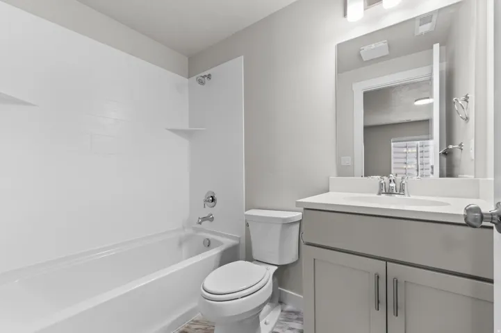 Bathroom featuring a white tub-shower combination with chrome fixtures, a gray vanity with a single sink, a large mirror, and light gray wall paint