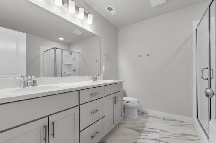 Dual vanity with white undermount sinks and chrome faucets, set against a large wall mirror with a brushed nickel light fixture