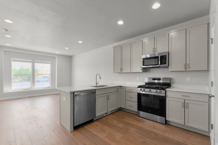 Modern kitchen featuring light gray cabinetry, stainless steel appliances, white countertops, and wood-finish flooring
