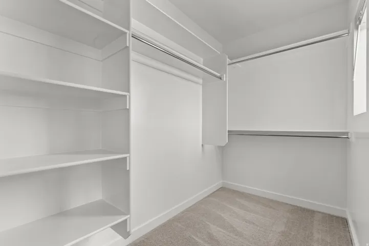 Walk-in closet with integrated white shelving, multiple hanging rods, and light gray carpet flooring
