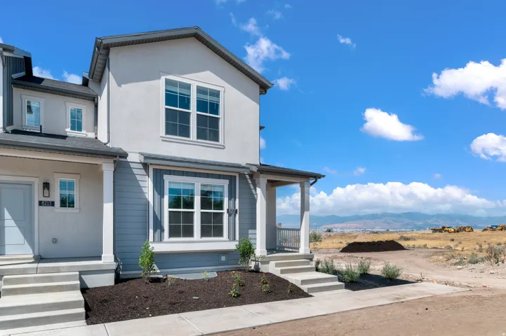 Contemporary townhouse exterior featuring a covered porch with white columns and railings, a two-tone facade with light grey stucco and blue siding, multi-pane windows, and a paved walkway leading to the entrance