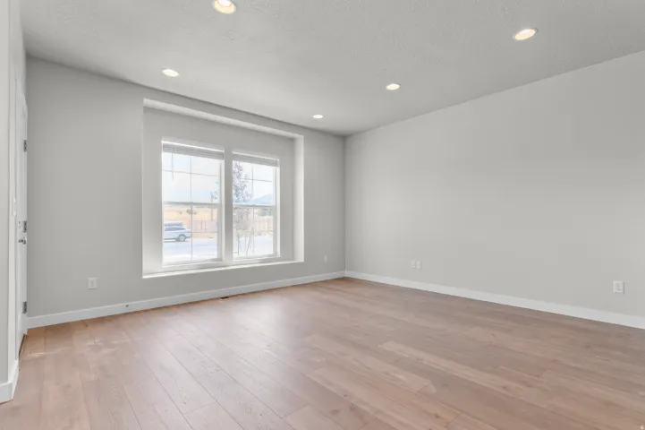 Spacious room featuring wood-finish flooring, recessed lighting, and a large window with white blinds