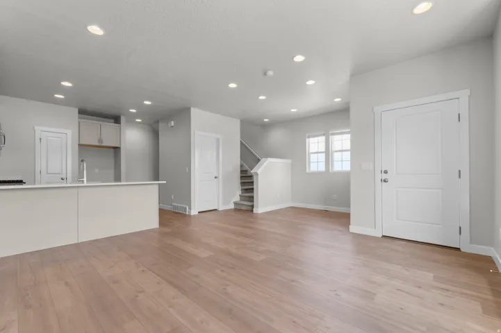 Spacious interior featuring wood-finish flooring, recessed lighting, a kitchen island with sink, white shaker cabinetry, and a carpeted staircase