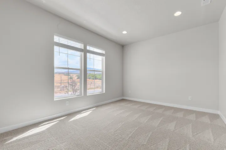 Spacious room featuring two large windows, recessed ceiling lighting, light-toned walls, and patterned carpet flooring