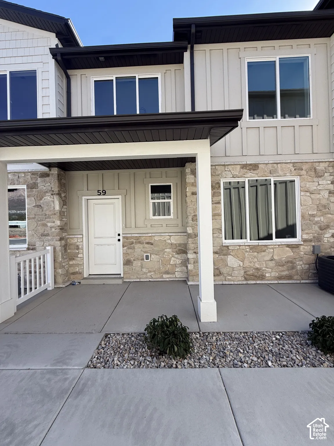 Stone facade, board and batten siding, multiple windows, covered porch, and concrete walkway