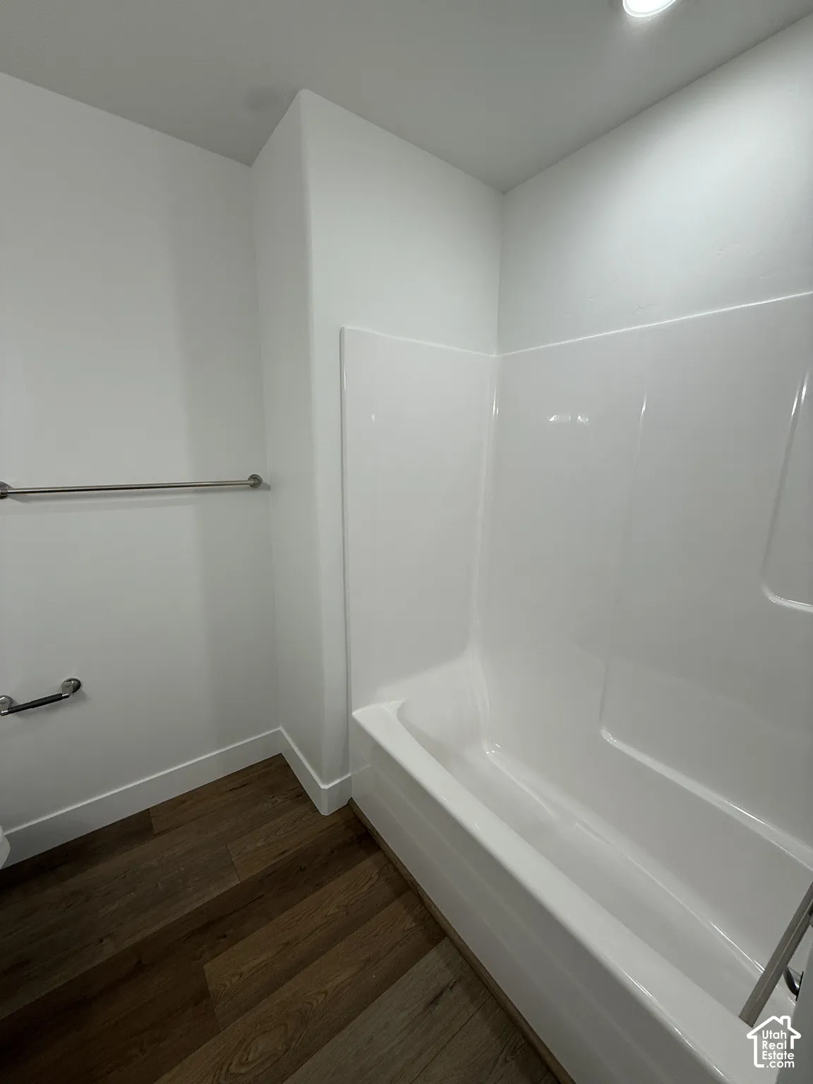 White bathtub with integrated shower, wood-finish flooring, and a stainless steel towel bar