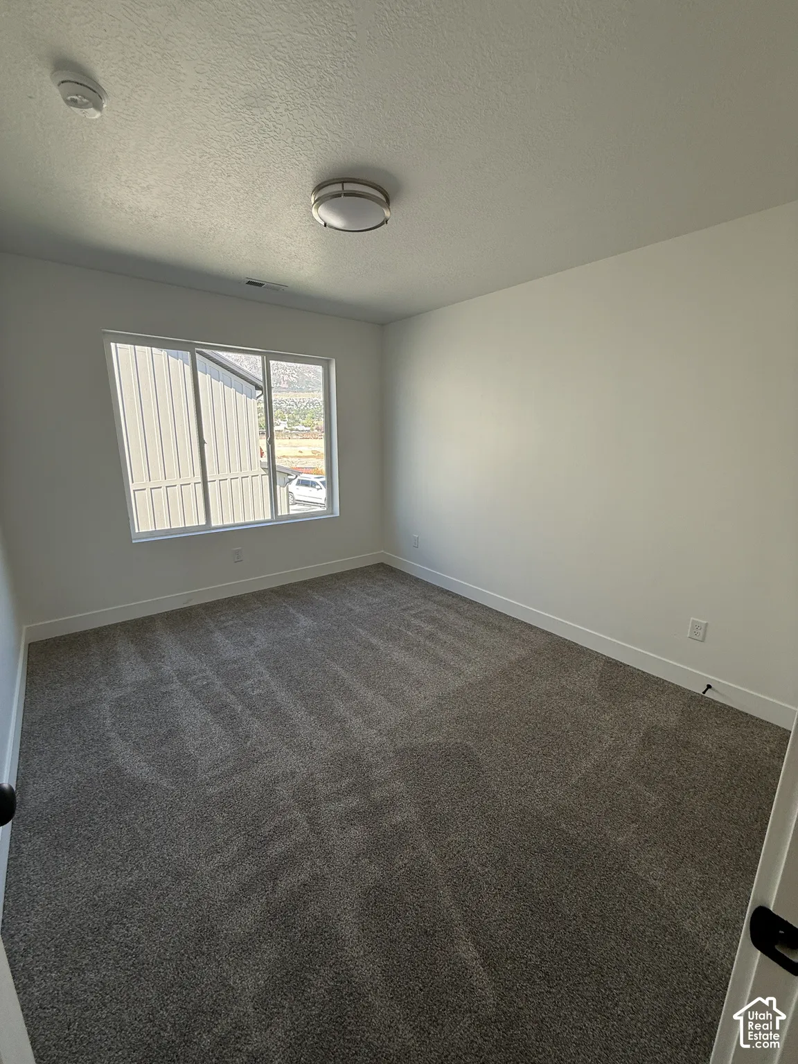 Recessed ceiling light, neutral wall paint, white trim, gray patterned carpeting, and a window with mountain scenery