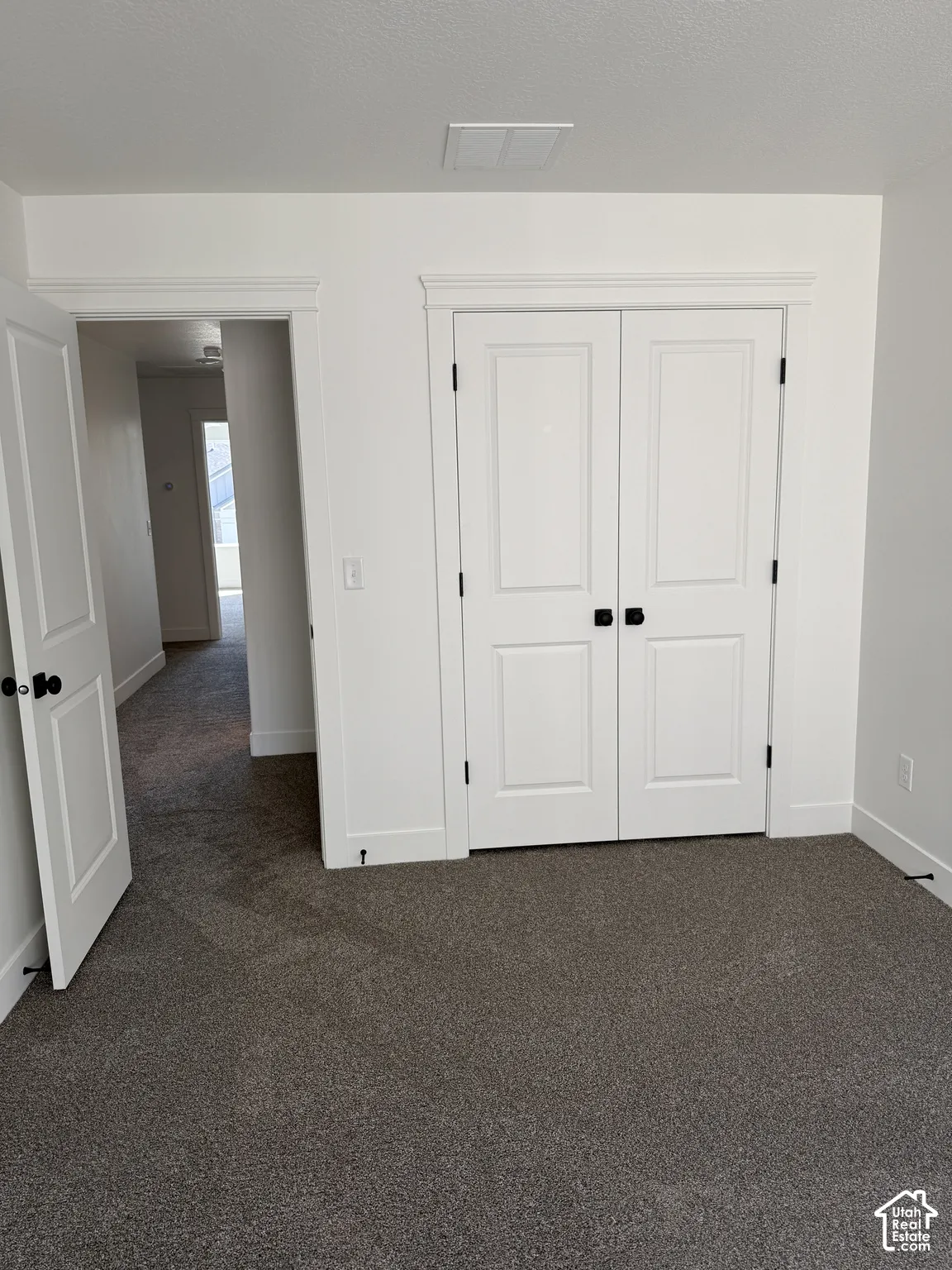 Plush gray carpeting, white trim, white paneled doors with black hardware, and a white ceiling