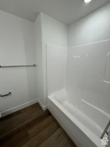 White bathtub with integrated shower, wood-finish flooring, and a stainless steel towel bar