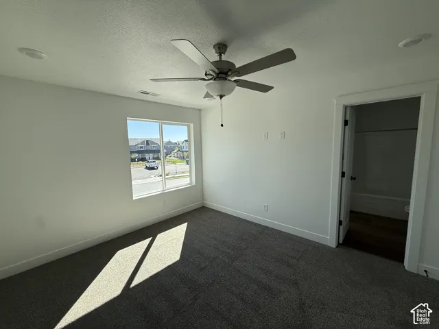 Recessed ceiling lighting, ceiling fan with integrated light, large window, dark gray carpeting, and white trim