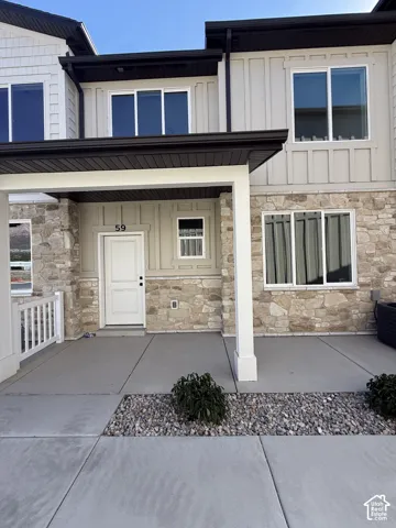 Stone facade, board and batten siding, multiple windows, covered porch, and concrete walkway