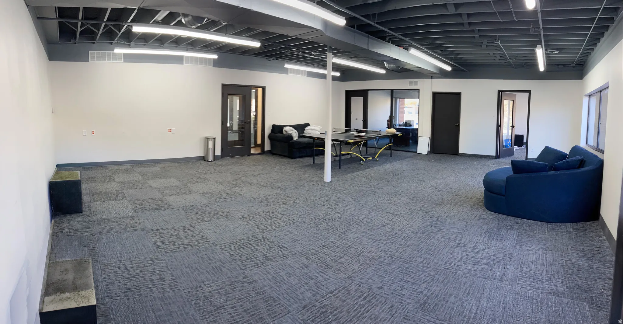 Spacious interior offering multiple rooms, featuring gray patterned carpet flooring, white walls, and an exposed dark ceiling