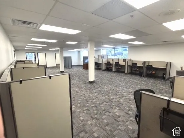 Open-concept office space featuring cubicles, patterned carpet flooring, drop ceiling with integrated lighting, and multiple windows