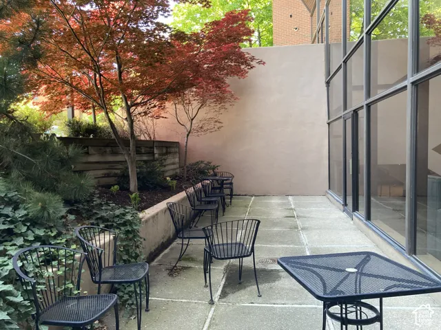 Private patio featuring concrete paver flooring, mature Japanese maples, a concrete retaining wall, and full-height windows