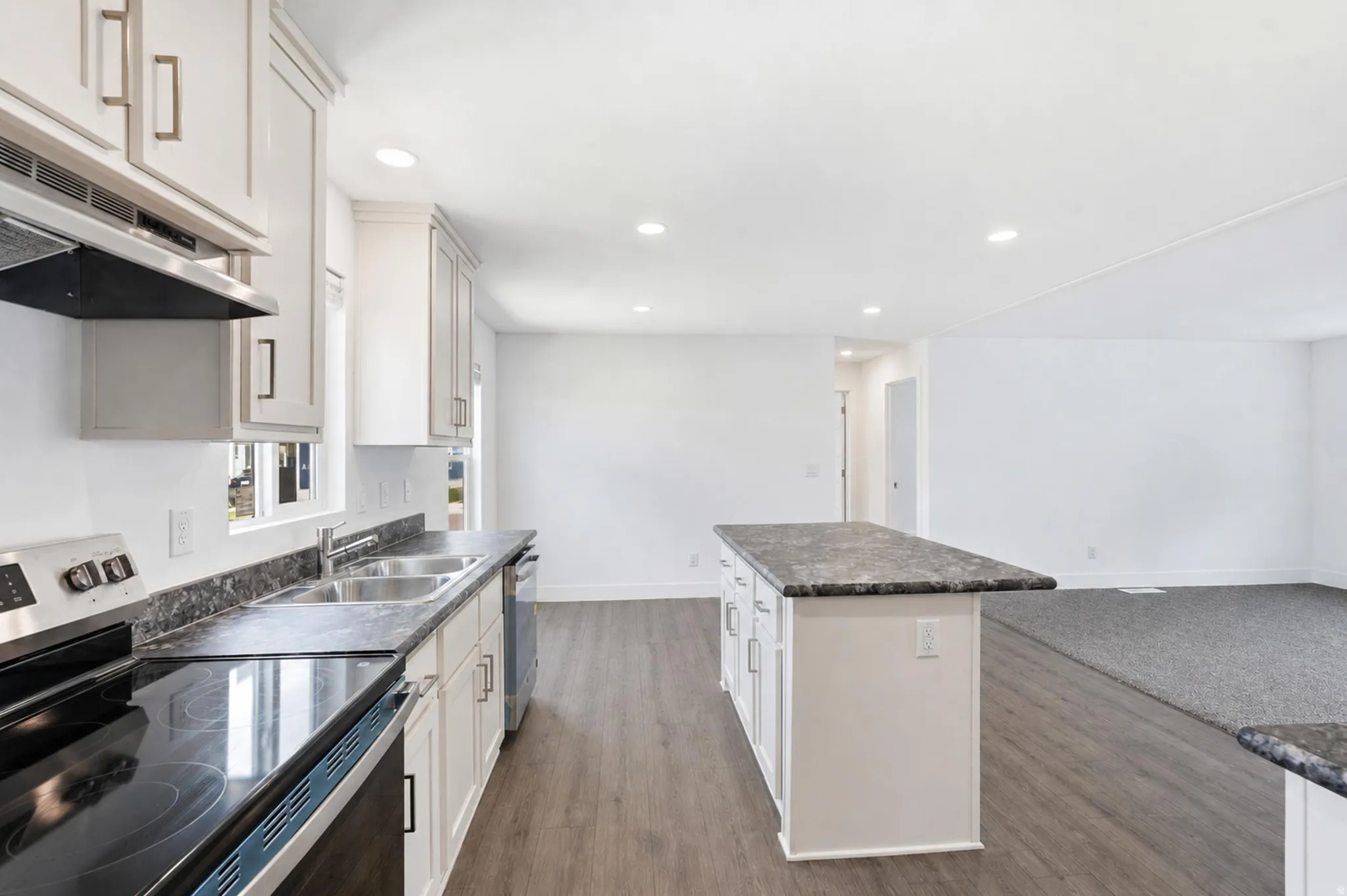 Kitchen with white cabinetry, dark speckled countertops, stainless steel appliances, and a central island