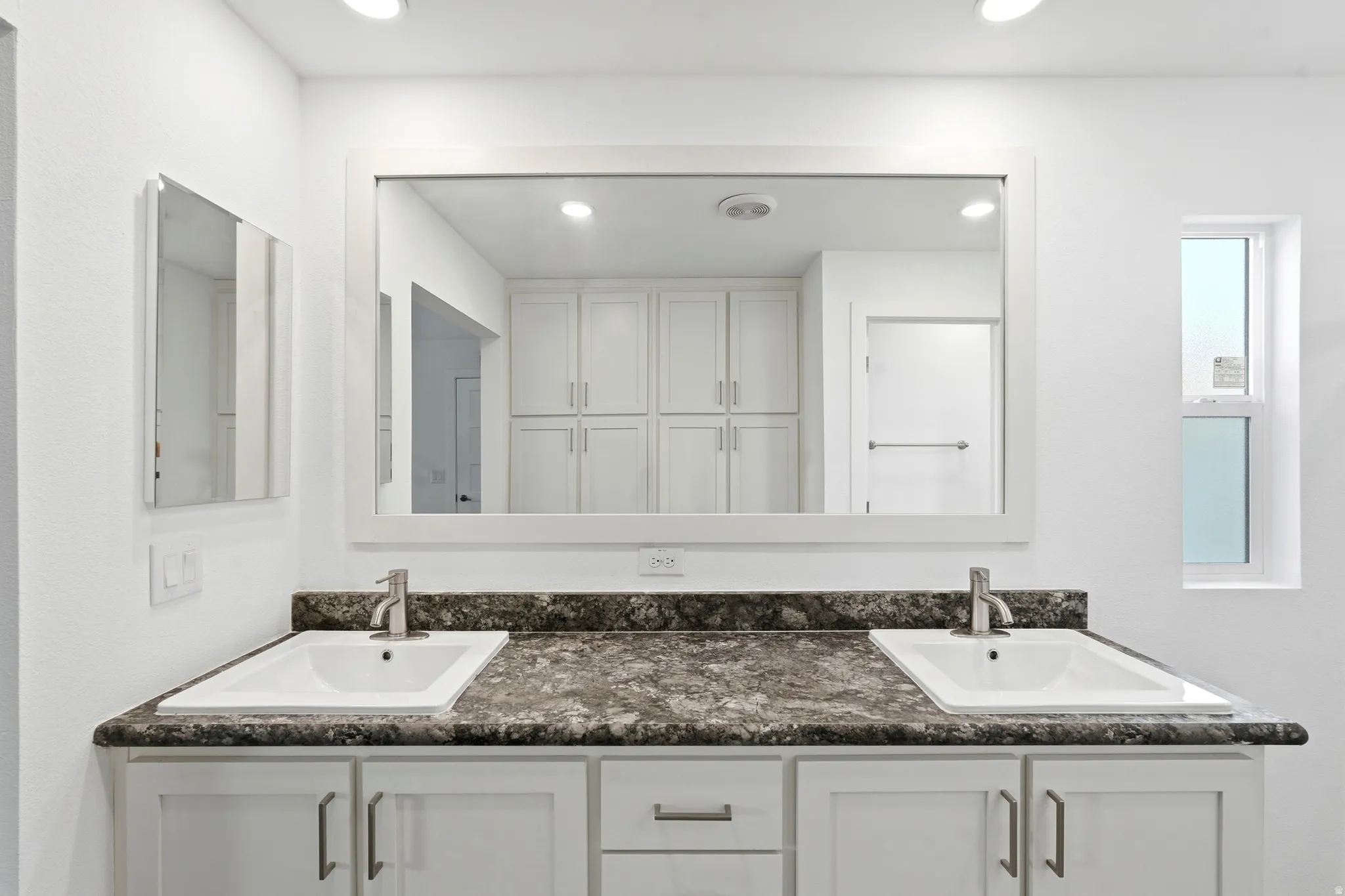 Dual vanity with integrated sinks, a dark speckled countertop, and white shaker-style cabinetry