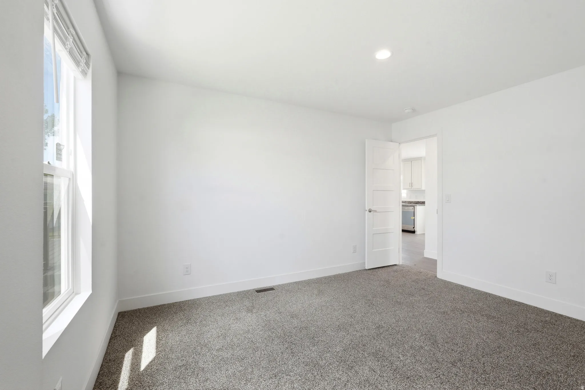 Carpeted room with white walls, recessed lighting, and a single window