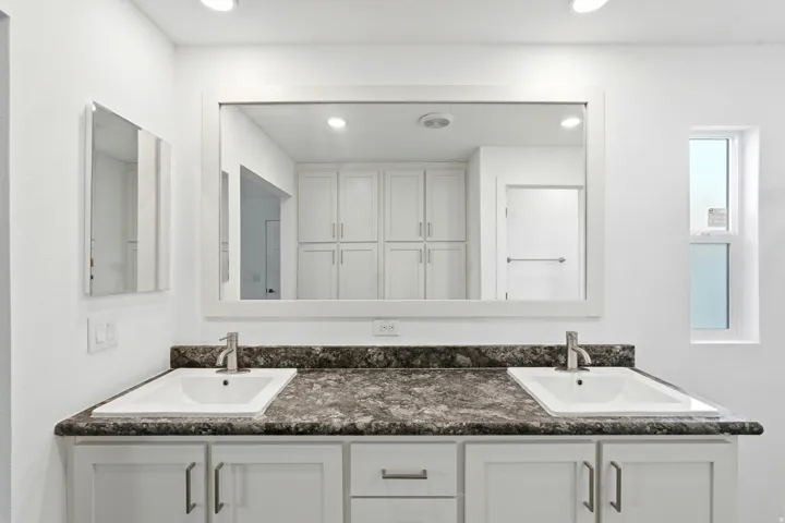 Dual vanity with integrated sinks, a dark speckled countertop, and white shaker-style cabinetry