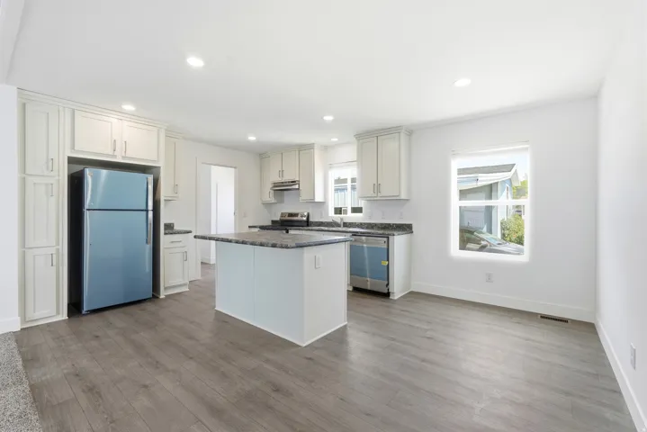 Open-concept kitchen and dining area featuring light-toned cabinetry, dark countertops, a central island, and wood-finish flooring