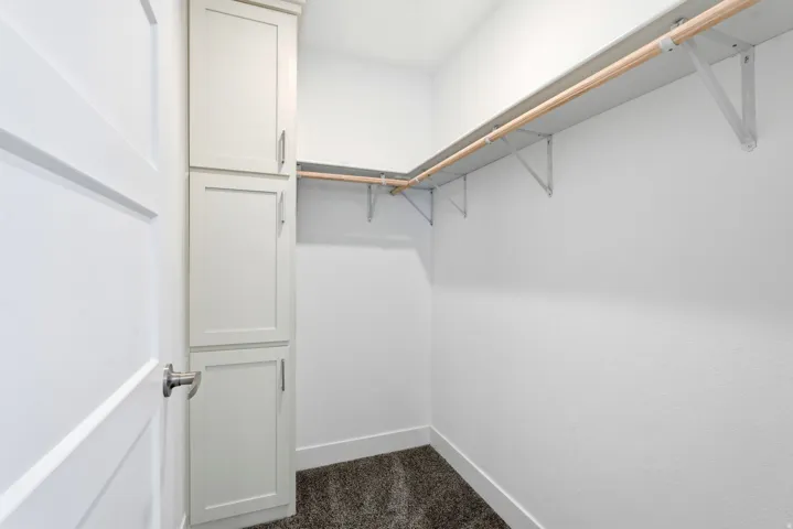 Walk-in closet featuring built-in cabinetry, an integrated hanging rod system, and dark carpet flooring