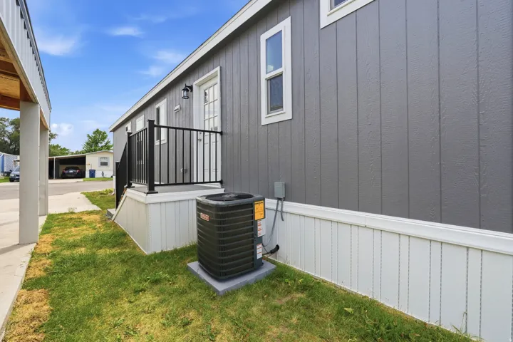 Exterior featuring gray vertical panel siding, white trim, and a covered entry with black metal railing