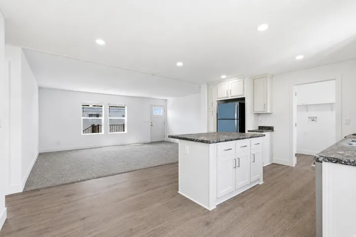 Open-concept living space featuring wood-finish flooring, recessed lighting, and a kitchen island with stone countertops