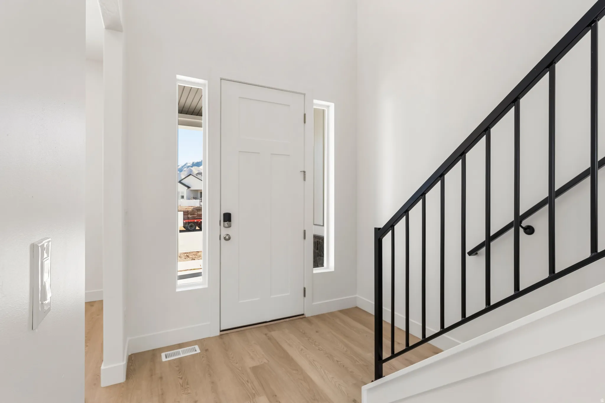 Entryway featuring a white paneled door with side windows, light wood-finish flooring, a black metal staircase railing, and white walls