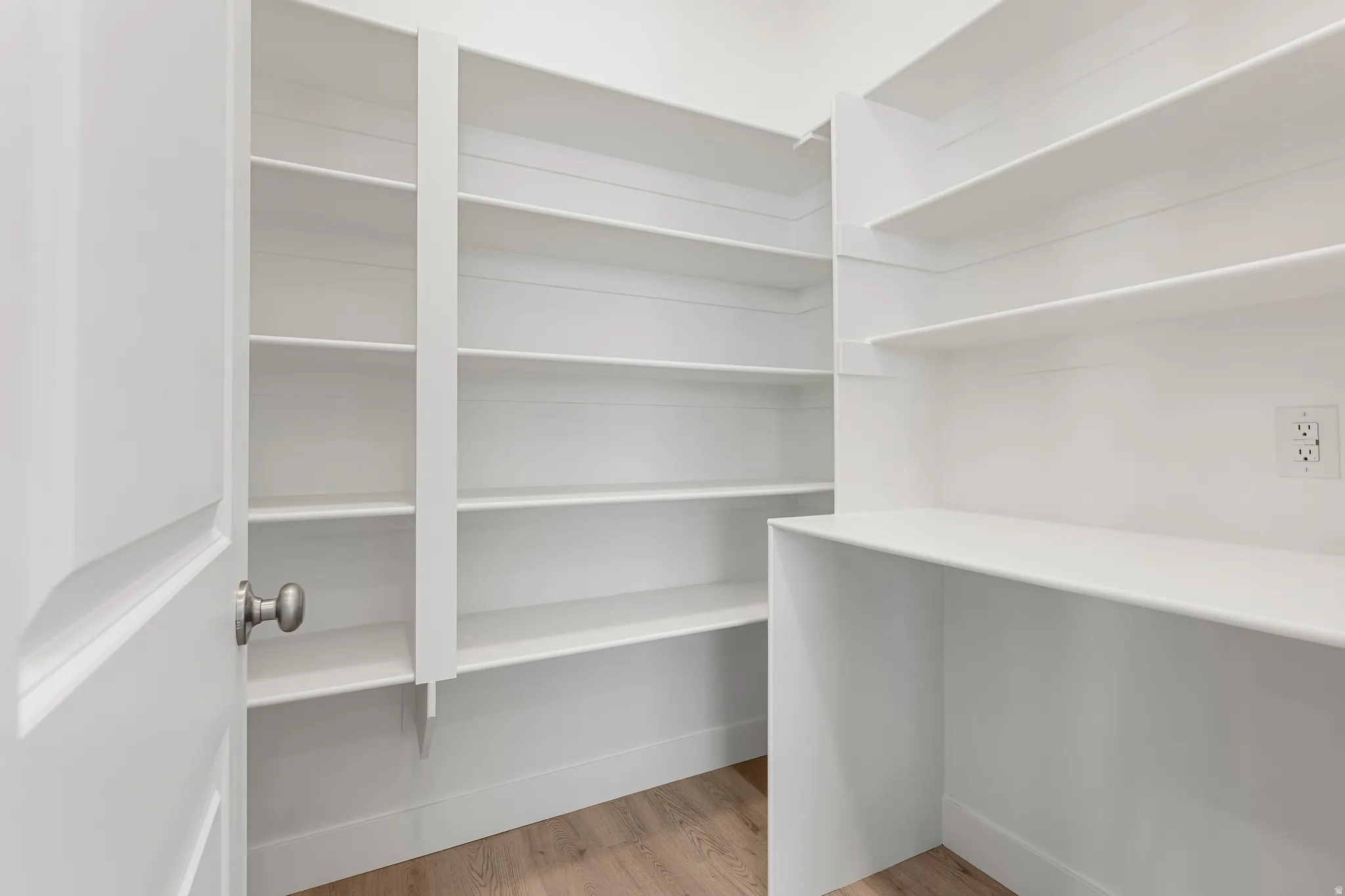 Walk-in pantry featuring extensive white shelving, a built-in countertop, and wood-finish flooring