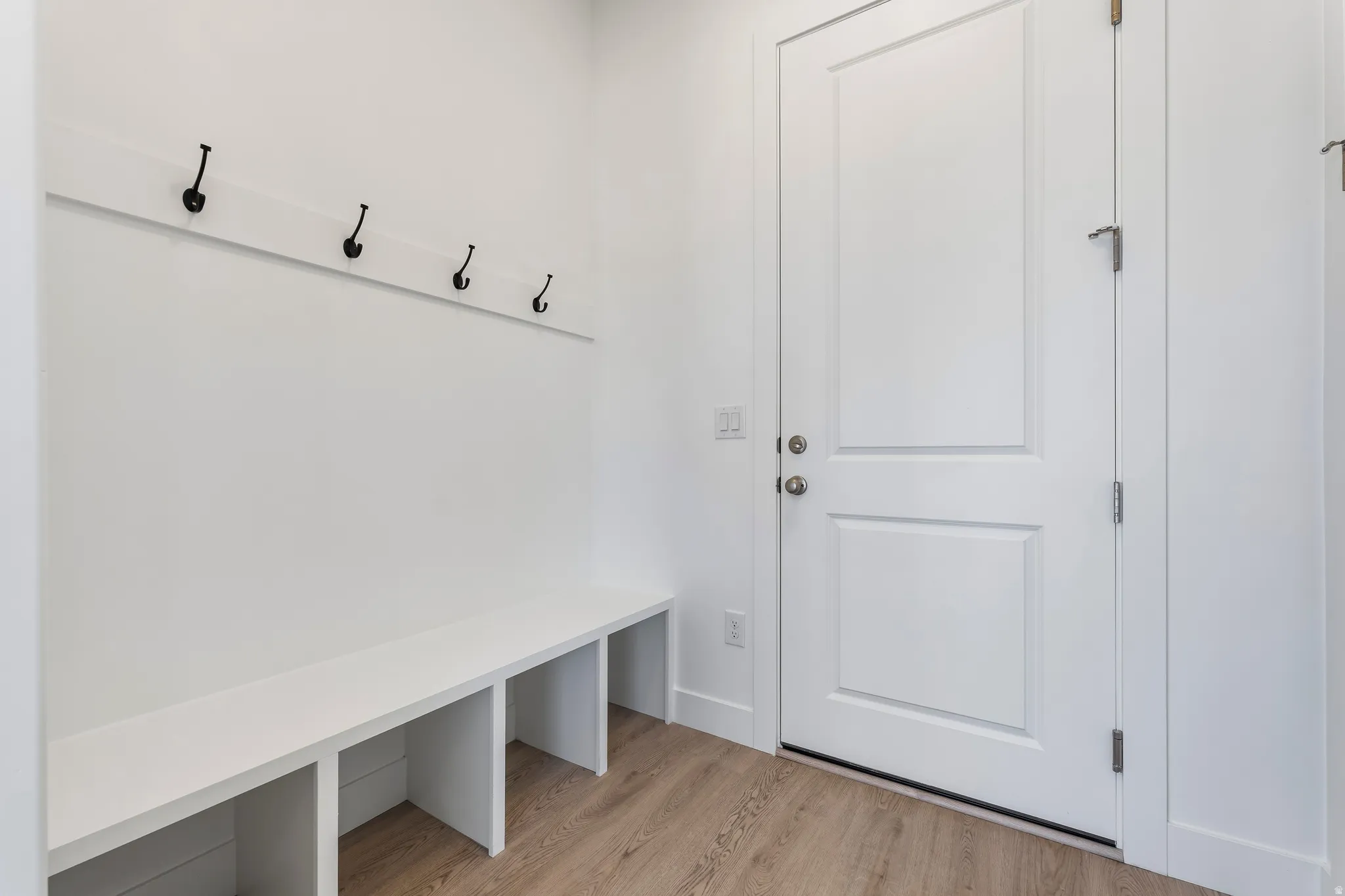 Entryway featuring a built-in bench with cubby storage, wall-mounted coat hooks, a paneled door with brushed nickel hardware, and wood-finish flooring