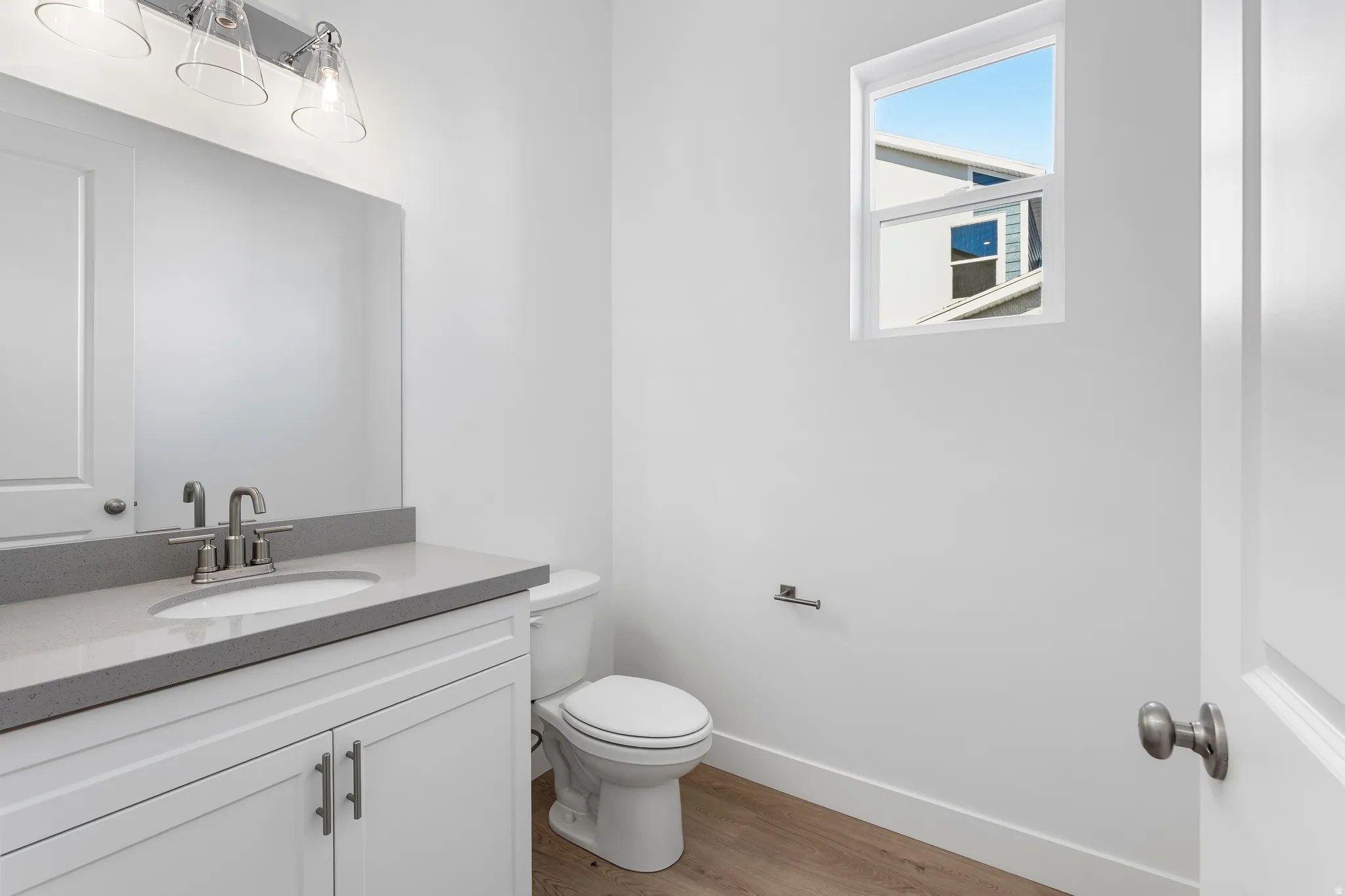 Modern bathroom featuring a white vanity with shaker-style cabinetry, a gray countertop, an undermount sink with a brushed nickel faucet, and wood-finish flooring
