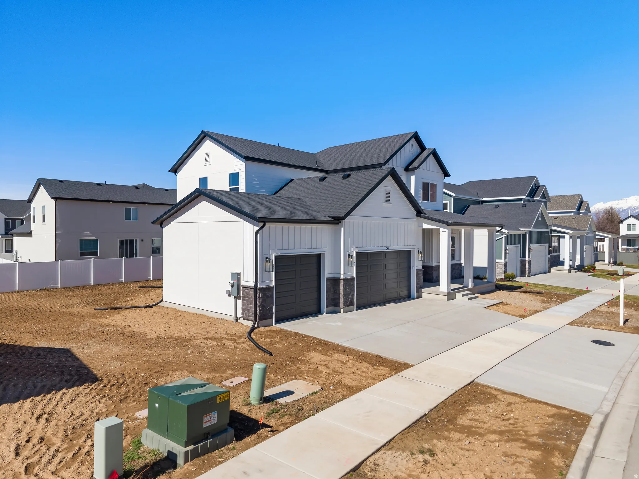 Contemporary two-story residence featuring a two-car garage, board and batten siding, dark stone accent details, and a covered porch entry