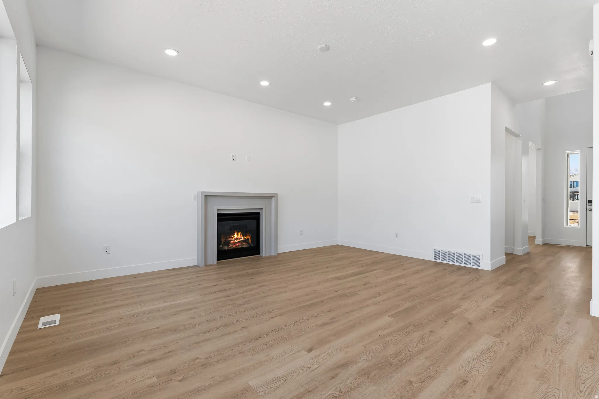 Expansive living area featuring a modern fireplace with a light-toned surround, wood-finish flooring, recessed lighting, and high vaulted ceilings