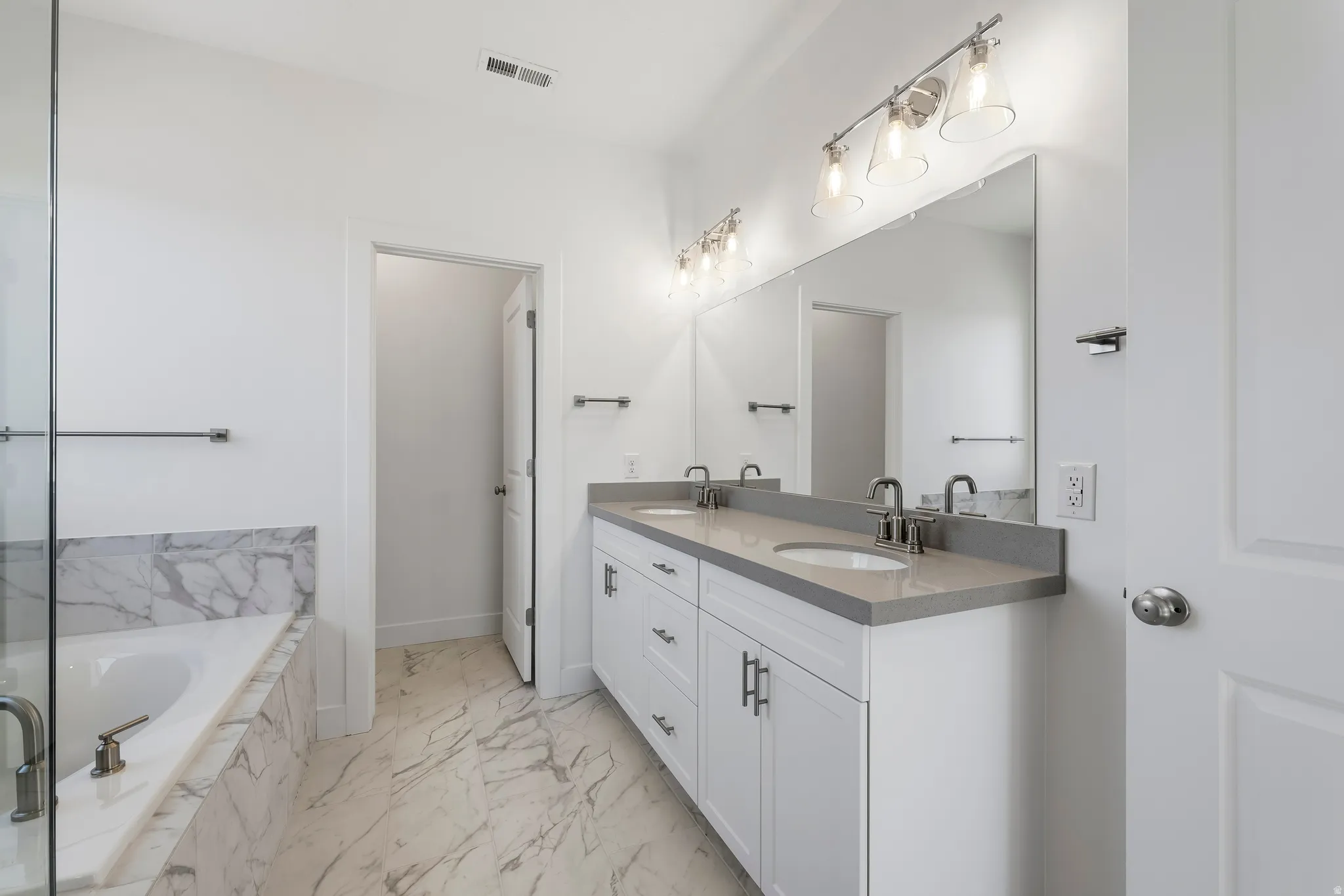 Spacious bathroom featuring a dual vanity with a light-toned countertop, a large mirror, and overhead lighting fixtures