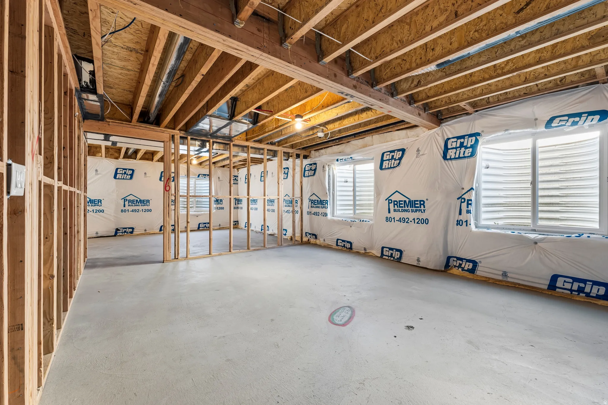 Unfinished lower level with wood framing, exposed ceiling joists, concrete flooring, and multiple window openings