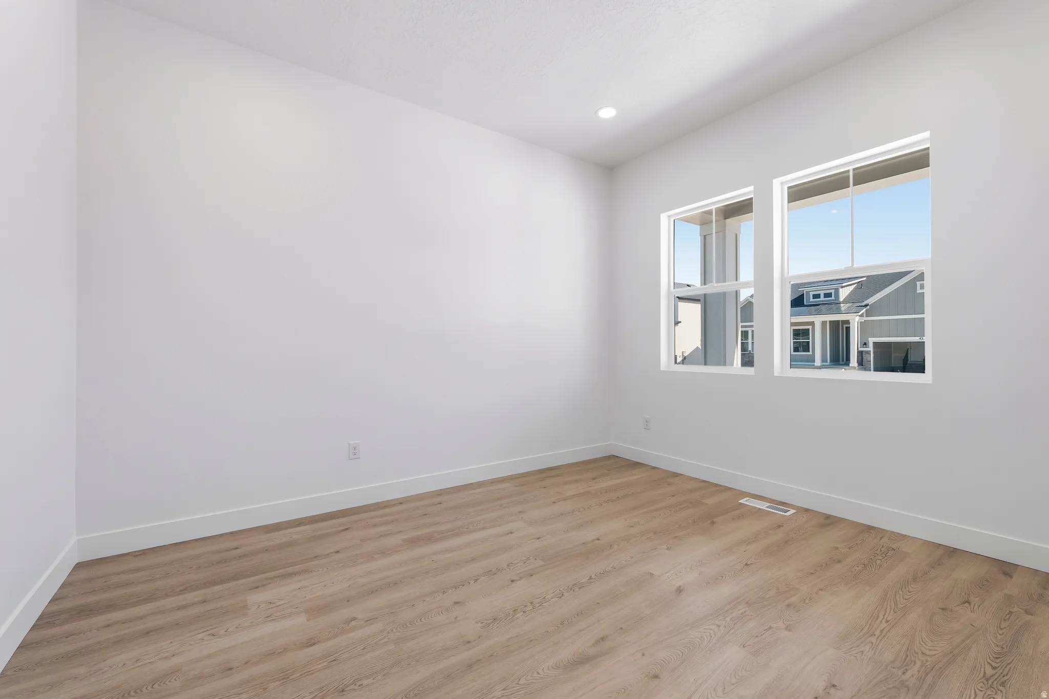 Bright interior room featuring wood-finish flooring, white baseboards, and clean white walls