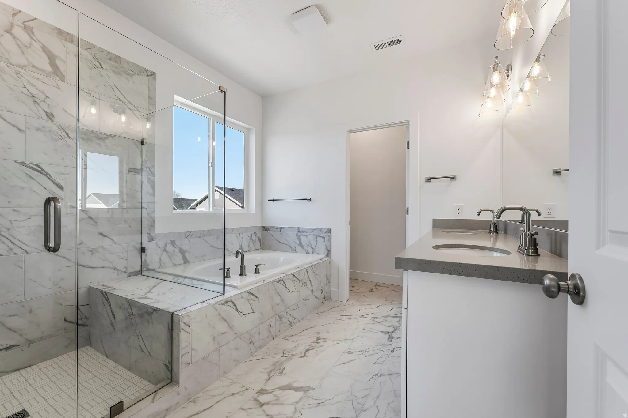Bathroom featuring a large soaker tub, glass-enclosed shower with tile surround, dual vanity with undermount sinks, and contemporary light fixtures