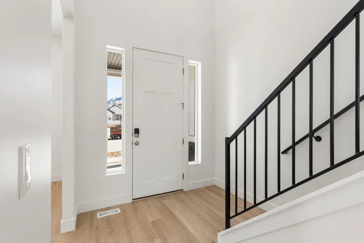 Entryway featuring a white paneled door with side windows, light wood-finish flooring, a black metal staircase railing, and white walls
