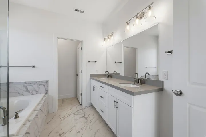 Spacious bathroom featuring a dual vanity with a light-toned countertop, a large mirror, and overhead lighting fixtures