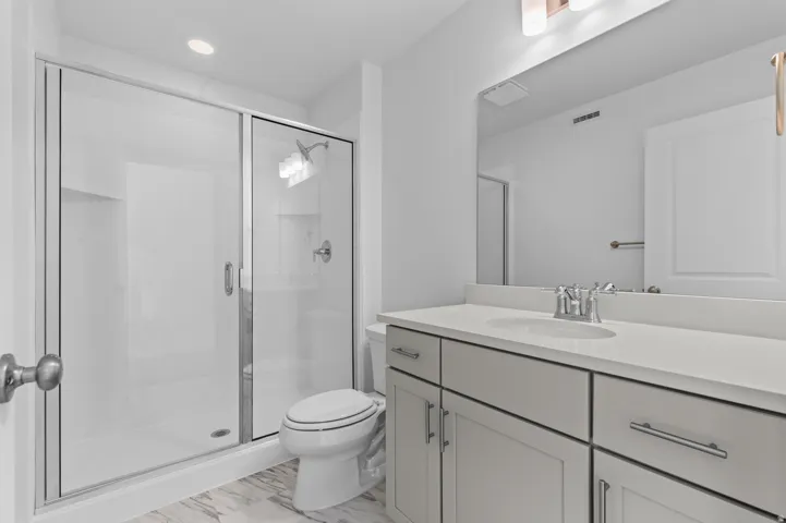 Shower with sliding glass enclosure, light gray vanity with an integrated sink, polished chrome faucet, full-width mirror, and overhead vanity lighting