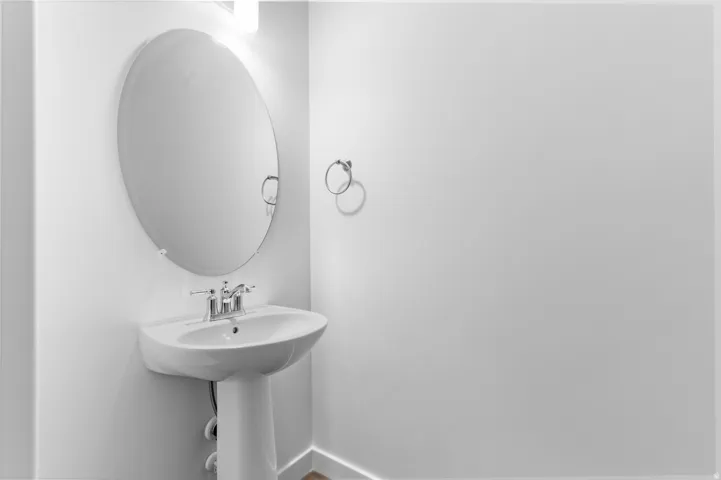 White pedestal sink with chrome faucet, complemented by an oval wall mirror and wall-mounted light fixture