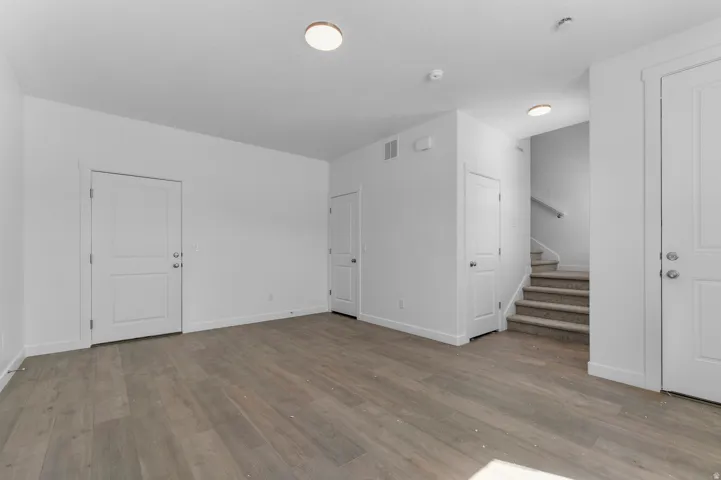 Wood-finish flooring, white walls, flush mount lighting, interior doors with satin nickel hardware, and a carpeted staircase with a handrail