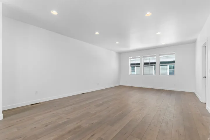 Recessed lighting, wood-finish flooring, multiple windows with blinds, and white walls
