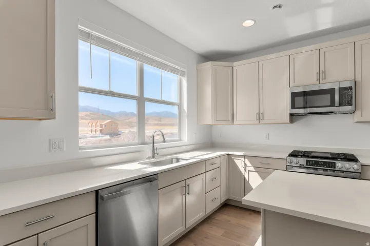 Kitchen featuring light-toned cabinetry, stainless steel appliances, a large sink, light-toned countertops, and wood-finish flooring