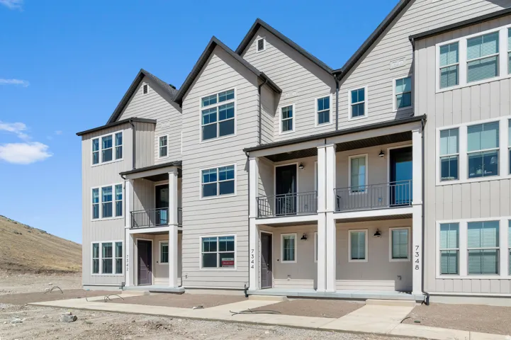 Contemporary townhome exterior featuring light-colored siding, black-framed windows, multiple balconies with dark railings, and a dark shingle roof